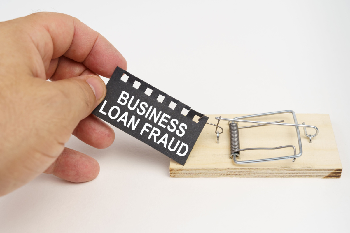 Hand holding business loan fraud written on paper and attached to mousetrap