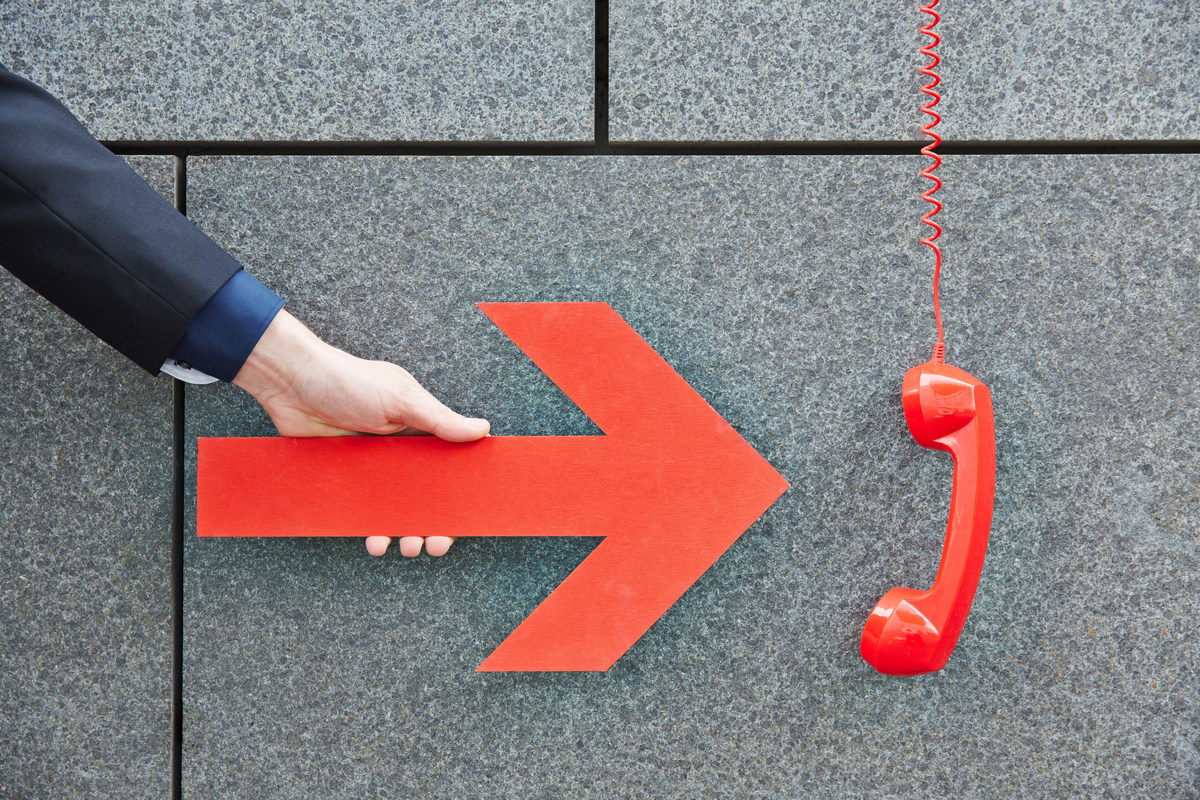 Man holding an arrow pointing at a red emergency phone.