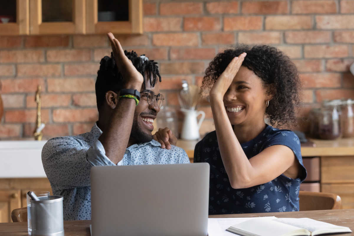 Happy excited Black man and Black woman celebrating financial success at laptop