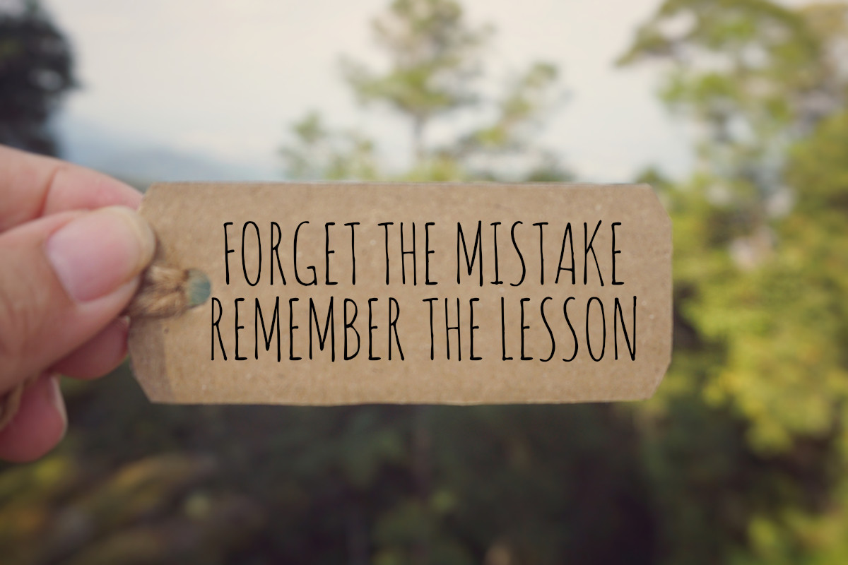 The phrase "Forget the mistakes, remember the lesson" printed on a piece of paper. 