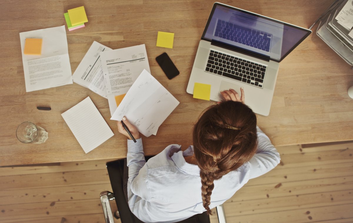 Business owner on laptop surrounded by paperwork.