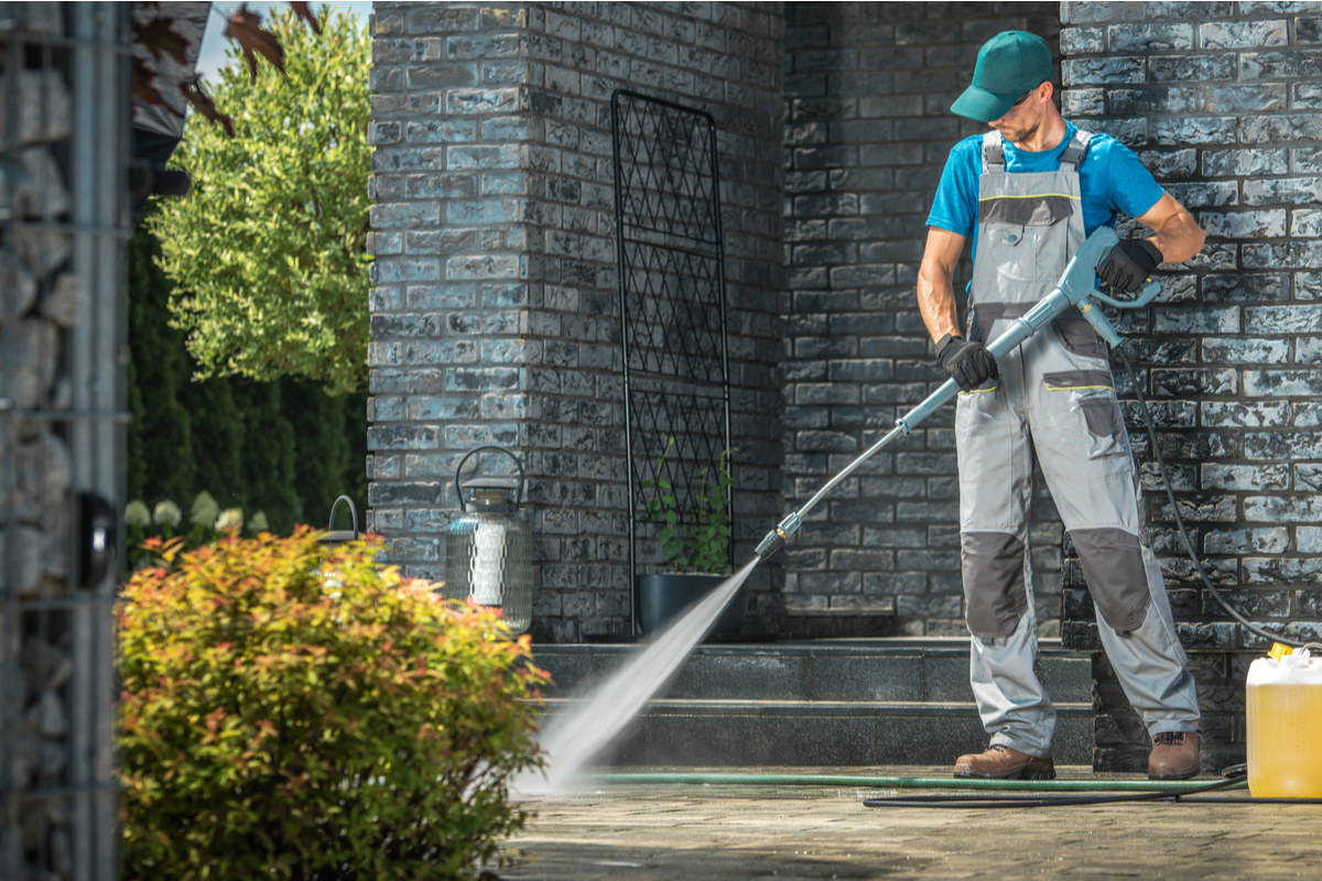 Man using a pressure washer to clean a driveway.