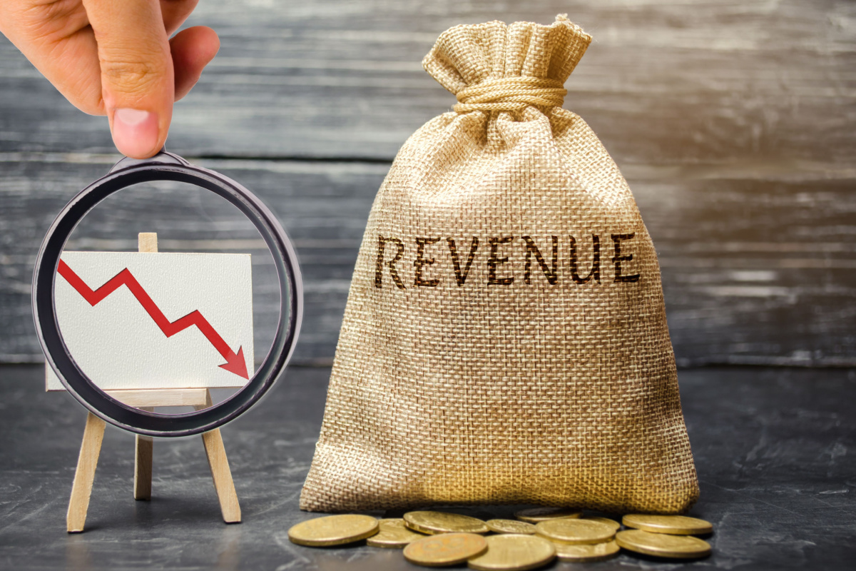 Magnifying glass on declining arrow next to bag with "Revenue" written on it