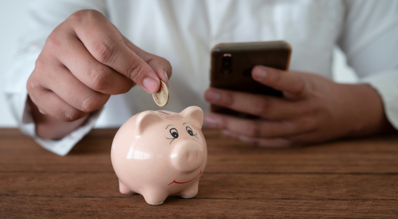 Man putting a single coin into a piggy bank.