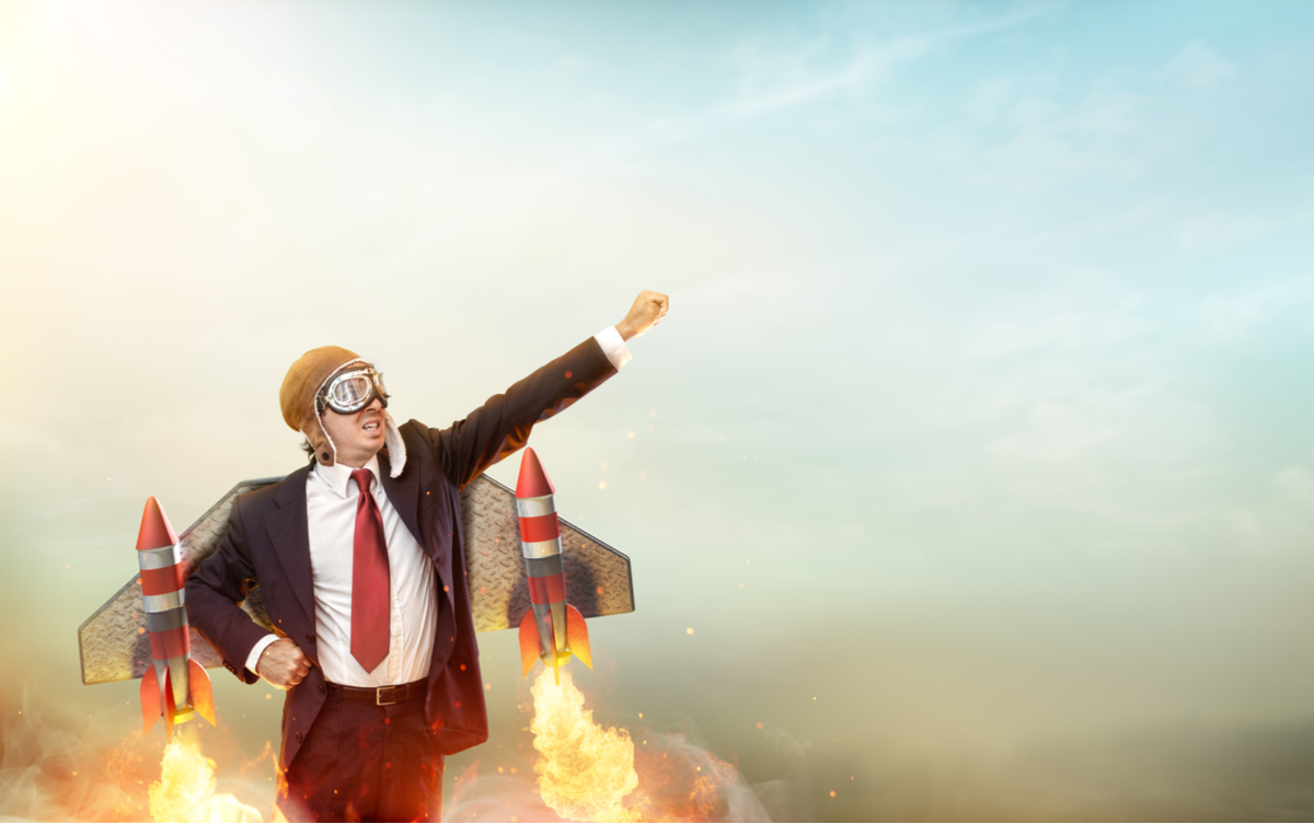 Businessman standing with rockets strapped to his back.