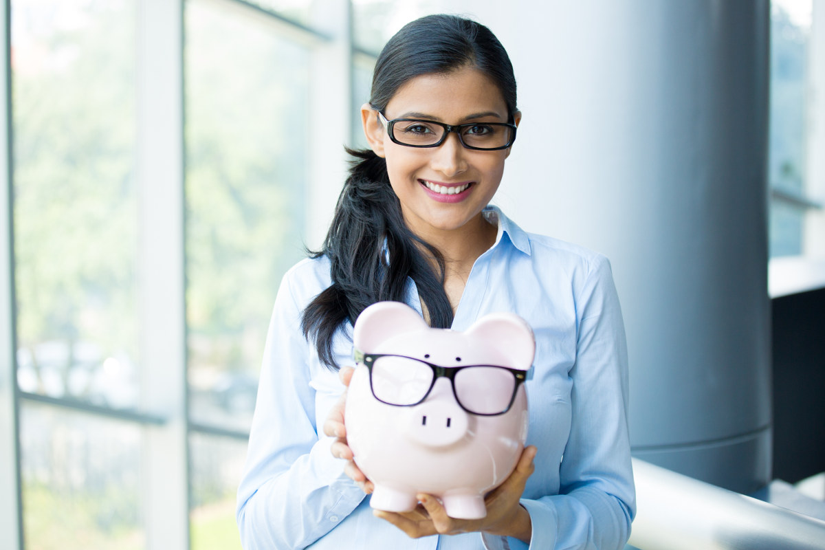 Woman holding a piggybank that's wearing glasses.