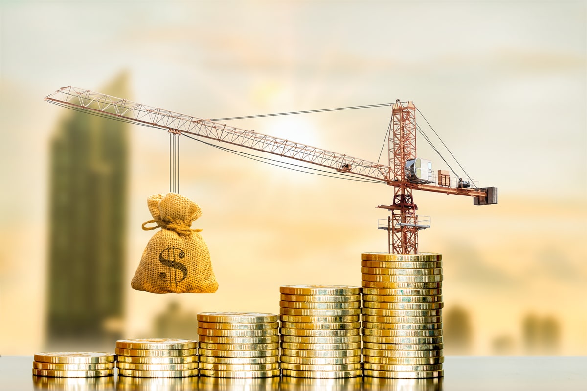 A construction crane on top of a stack of coins lifting a bag of money.